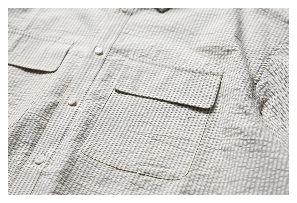 Close-up of the shirt front showing a flap chest pocket, button placket and fine dark stripes.