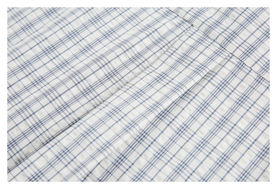 Close-up of cream fabric with a blue-gray plaid pattern and a stitched seam.