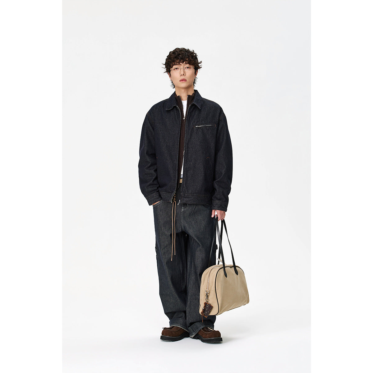 Full-length model wearing a dark indigo denim jacket with a zip chest pocket, wide-leg jeans and carrying a tan bag.