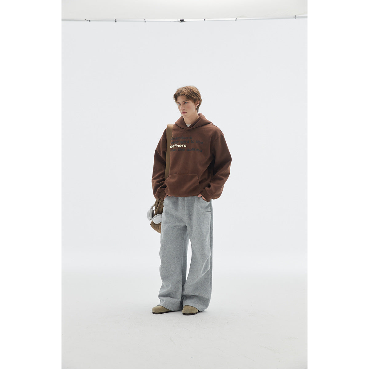 Full-length view of a model in a brown slogan-print hoodie and loose gray sweatpants.