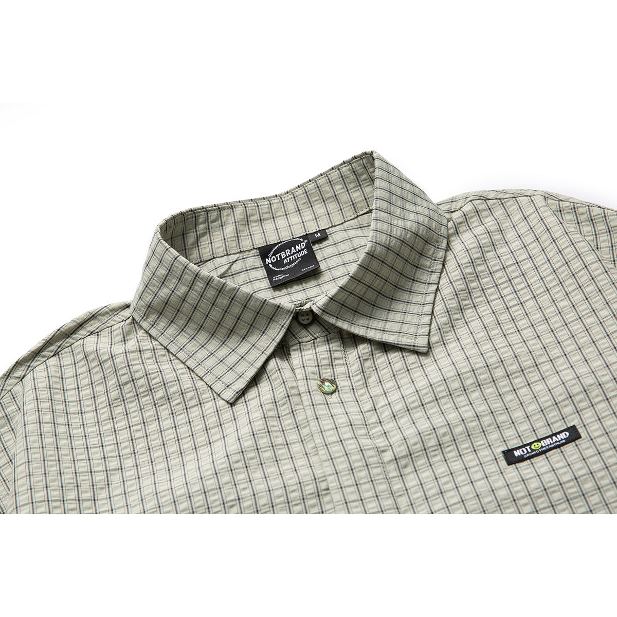 Close-up of a pale gray-green plaid shirt collar, buttons, neck label, and black chest patch.