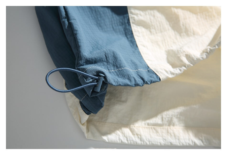 Close-up of a blue drawcord and toggle at the hem of a cream-and-blue garment.
