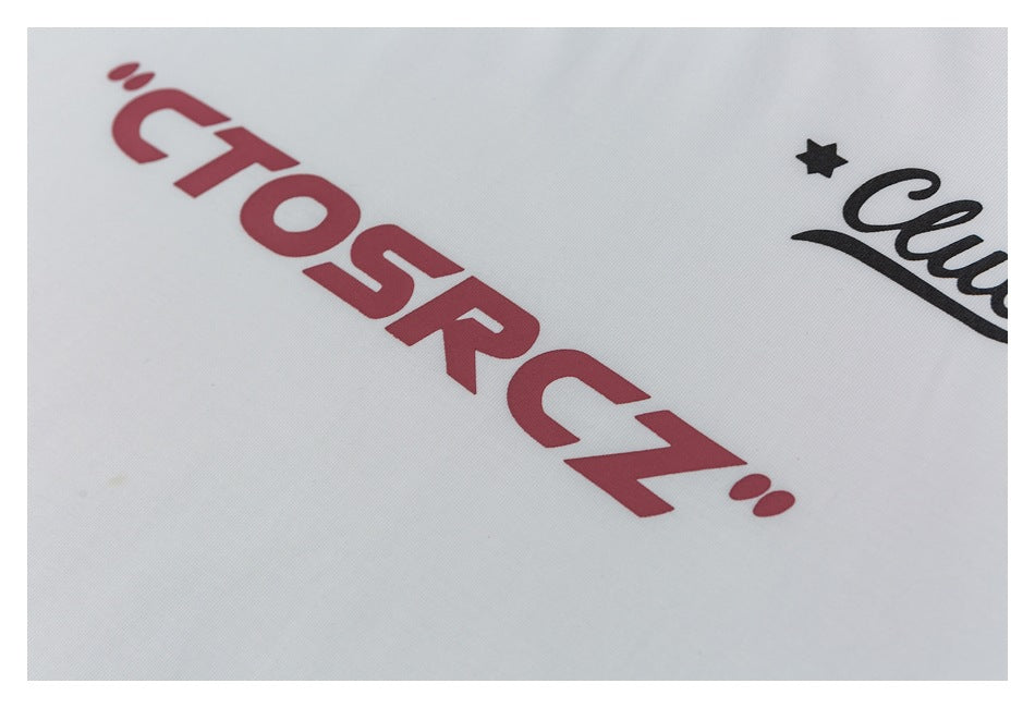 Close-up of red lettering and part of a black star-and-script graphic on white fabric.