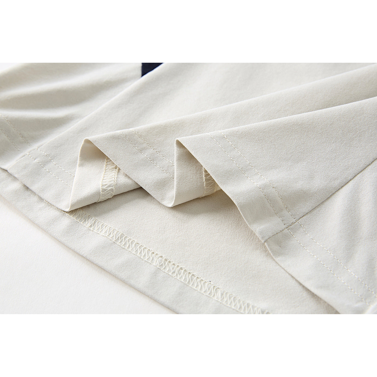 Close-up of the ivory T-shirt hem showing folded stitching and overlocked seams.