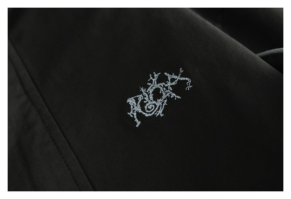 Close-up of a small silver embroidered motif on black fabric.