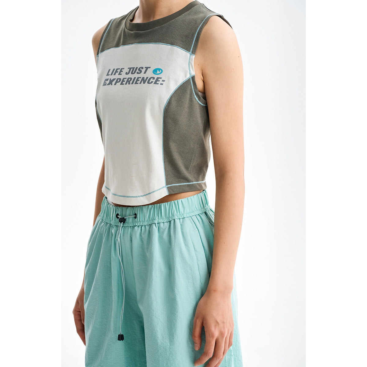 Close view of a model wearing a gray and white color-block sleeveless crop top with aqua piping and mint shorts.
