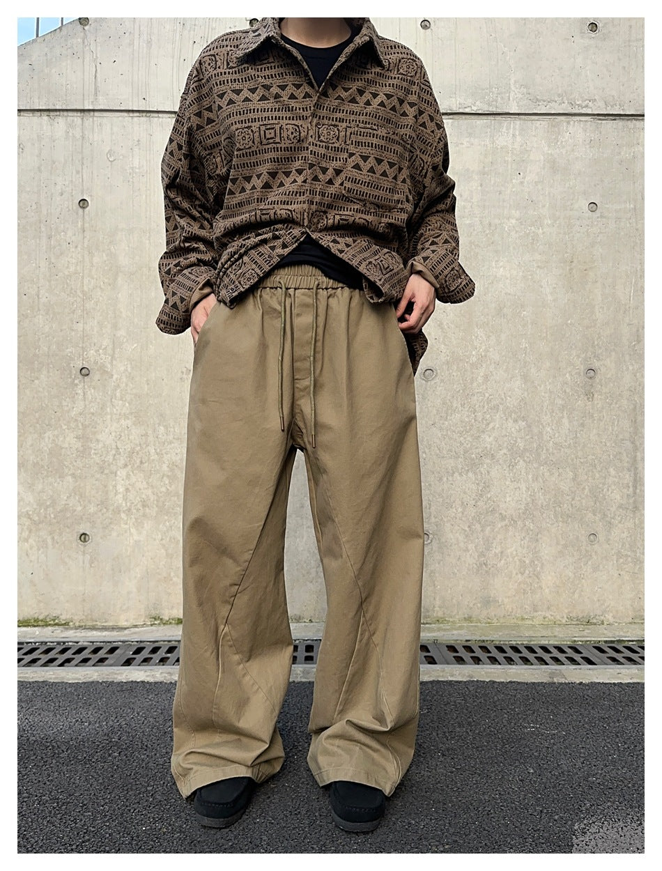Front view of a model wearing taupe wide-leg drawstring pants with a patterned brown overshirt.
