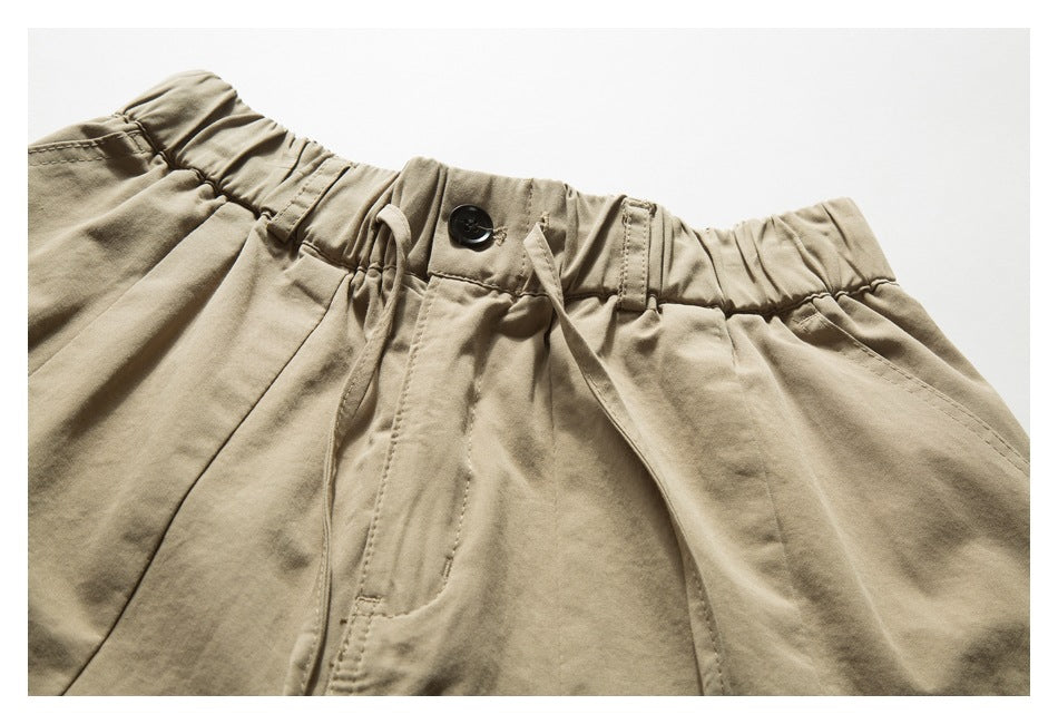 Close-up of khaki shorts showing an elastic waistband, button, drawcord, belt loops, and front pocket seams.