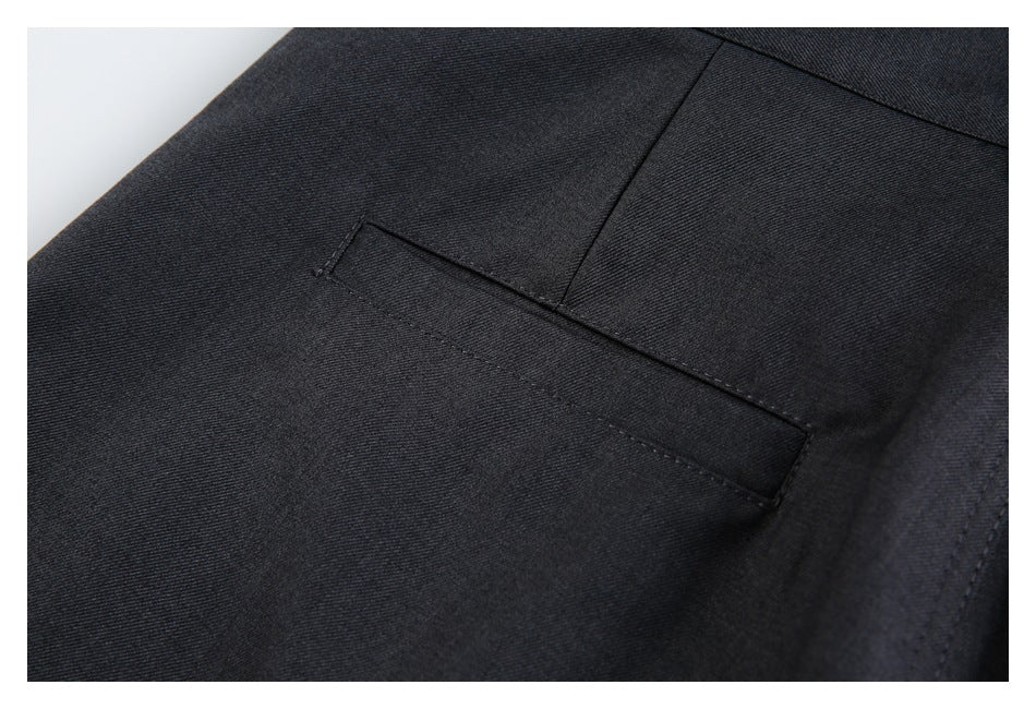 Close-up of charcoal trousers showing a narrow welt pocket and surrounding seams.