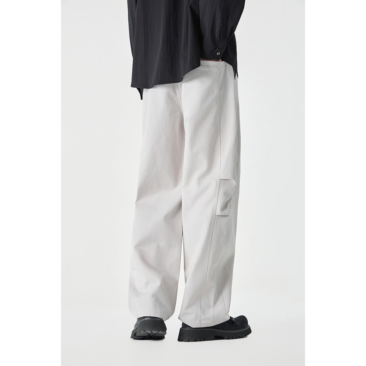 Rear view of a cropped model wearing loose light gray wide-leg pants and black shoes.