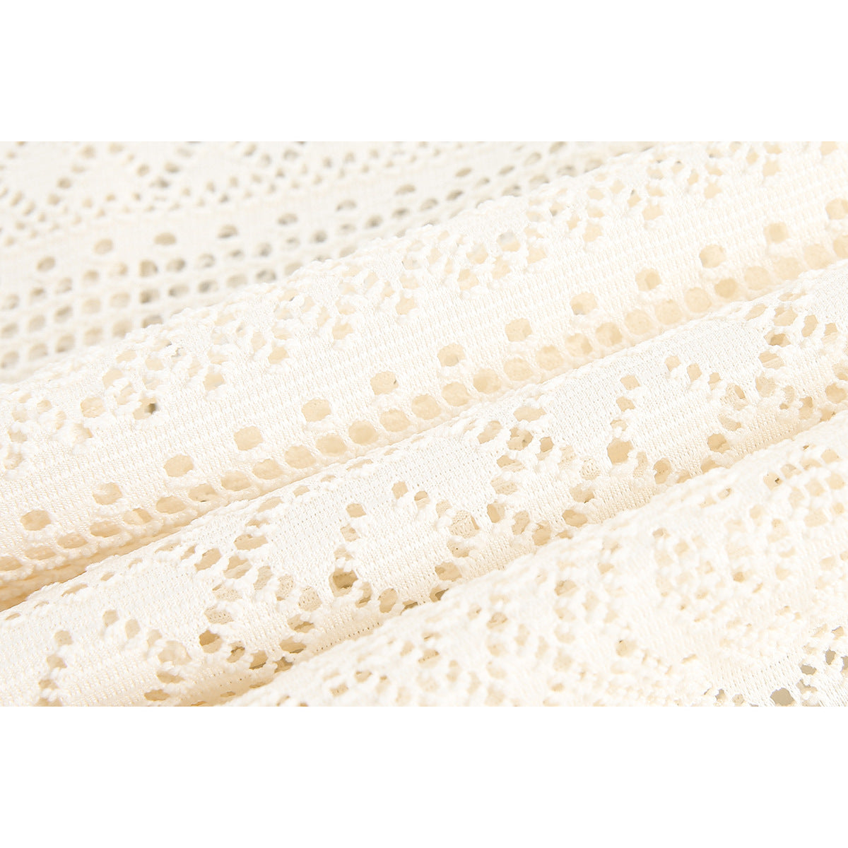 Macro view of cream openwork fabric with rows of geometric patterns and small cutout details.