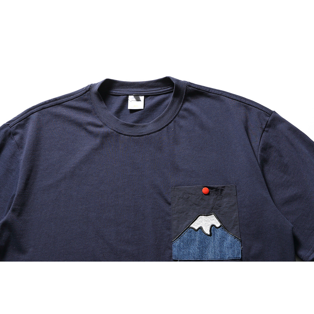 Close front view of a navy short-sleeve T-shirt with a chest pocket, red snap, and mountain appliqué.