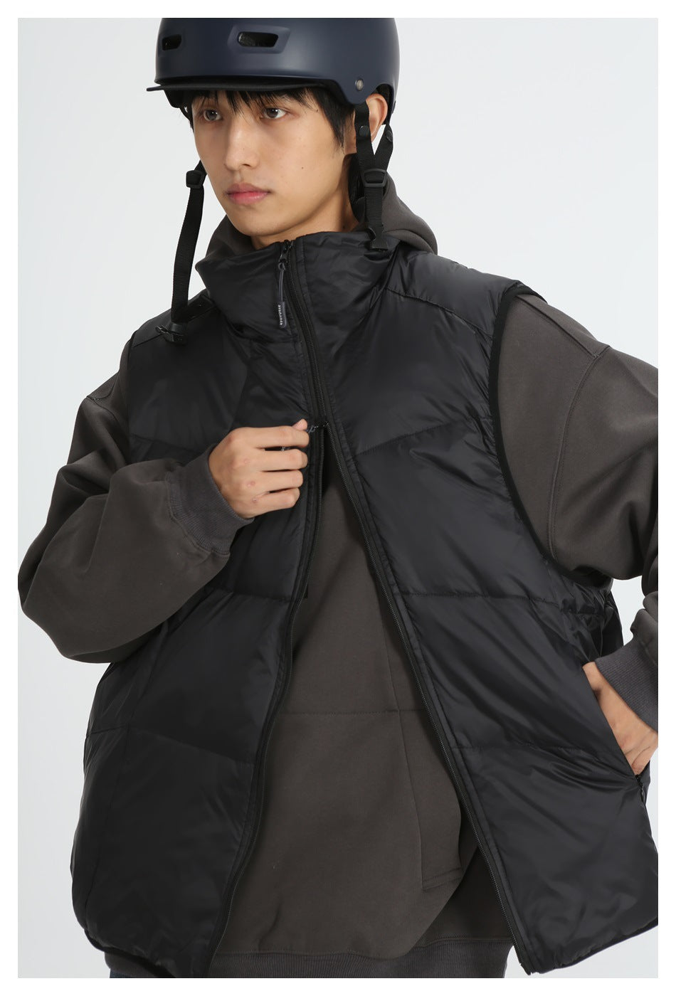 Person in a helmet wearing a black quilted stand-collar vest, half unzipped, over a dark gray hoodie