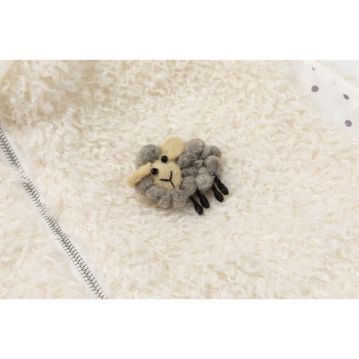 Close-up of a gray-and-yellow sheep applique on an ivory curly-fleece vest beside its zipper.
