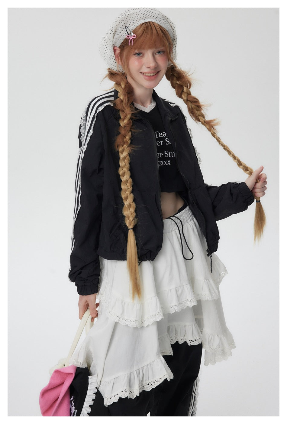 Closer front view of a model wearing a black jacket with white striped lace-trim sleeves and a white tiered skirt.