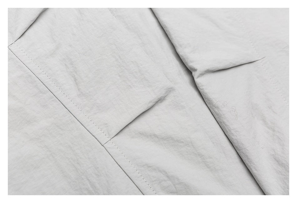 Close-up of light gray garment construction with stitched seams and overlapping folded fabric.