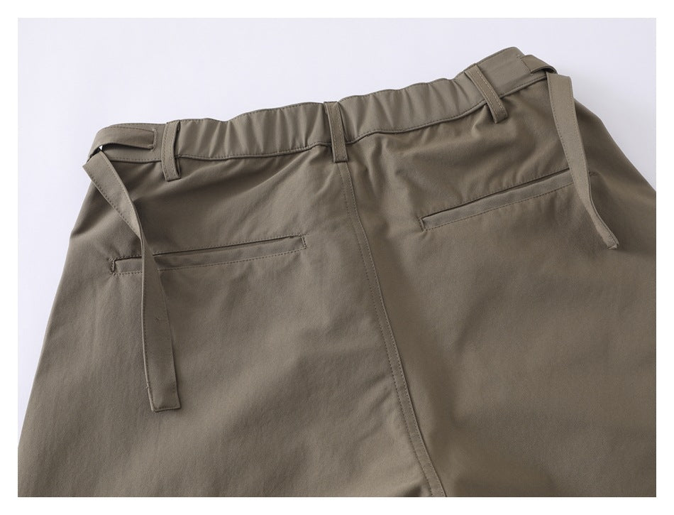 Back view of taupe trousers with belt loops, a gathered waistband, long waist ties and welt pockets.