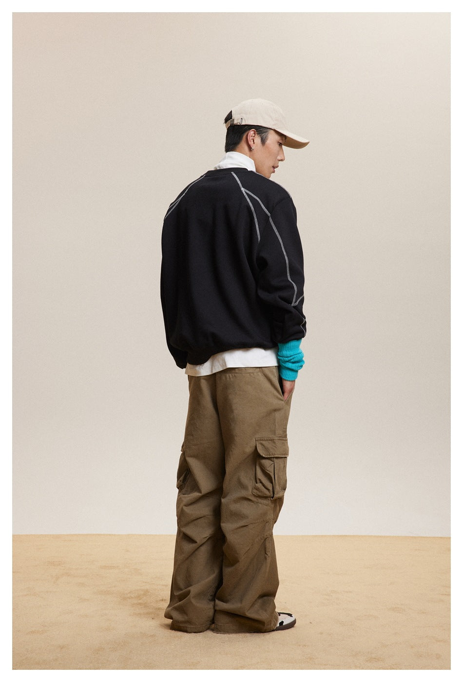 Back view of a model wearing a black sweatshirt with contrast seams and loose brown cargo pants.