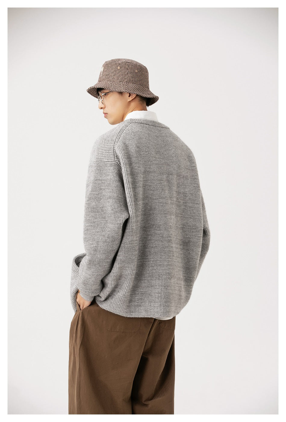 Back view of model wearing light gray waffle-knit cardigan with a bucket hat and brown pants