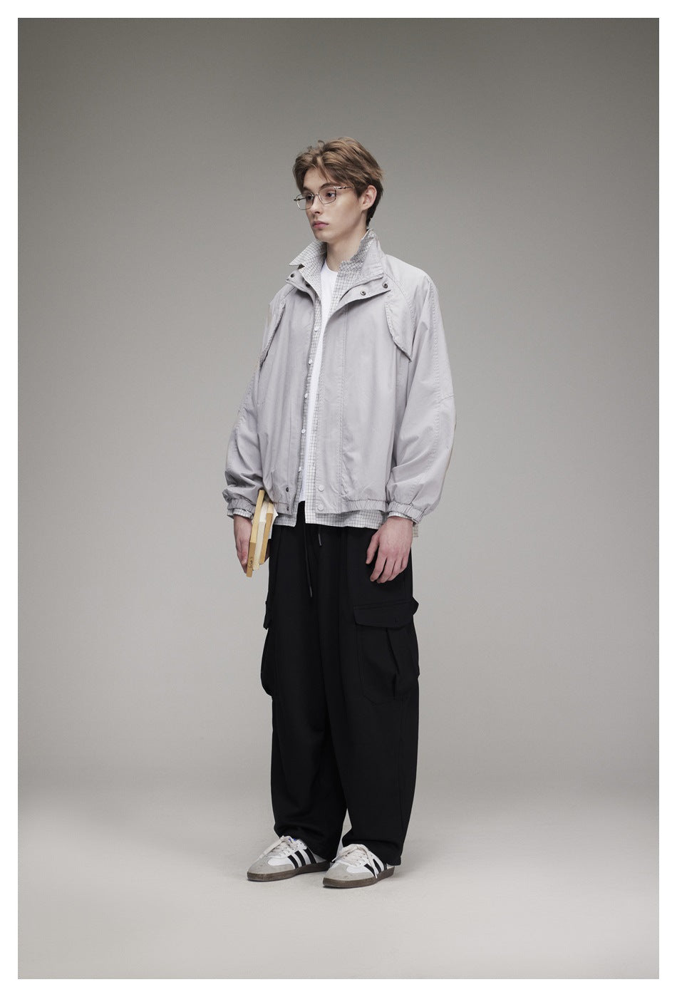 Model in a light gray stand-collar jacket over a checked shirt with black cargo pants, three-quarter side view