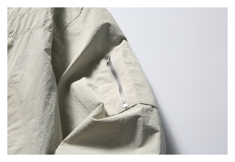 Close-up of the zippered utility pocket on the sleeve of a light stone-gray jacket.