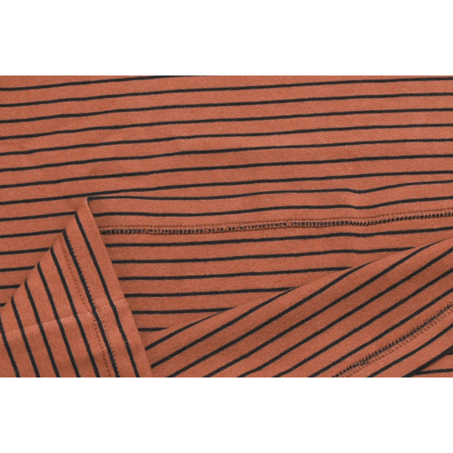 Close-up of rust-orange fabric with thin black stripes, showing a stitched seam and folded edge.