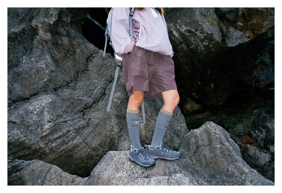 Side view of a hiker wearing mauve shorts and a pale jacket, standing on rocky ground.