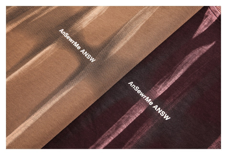 Close-up of brown and burgundy T-shirt fabric showing pale streaks and white printed chest lettering.