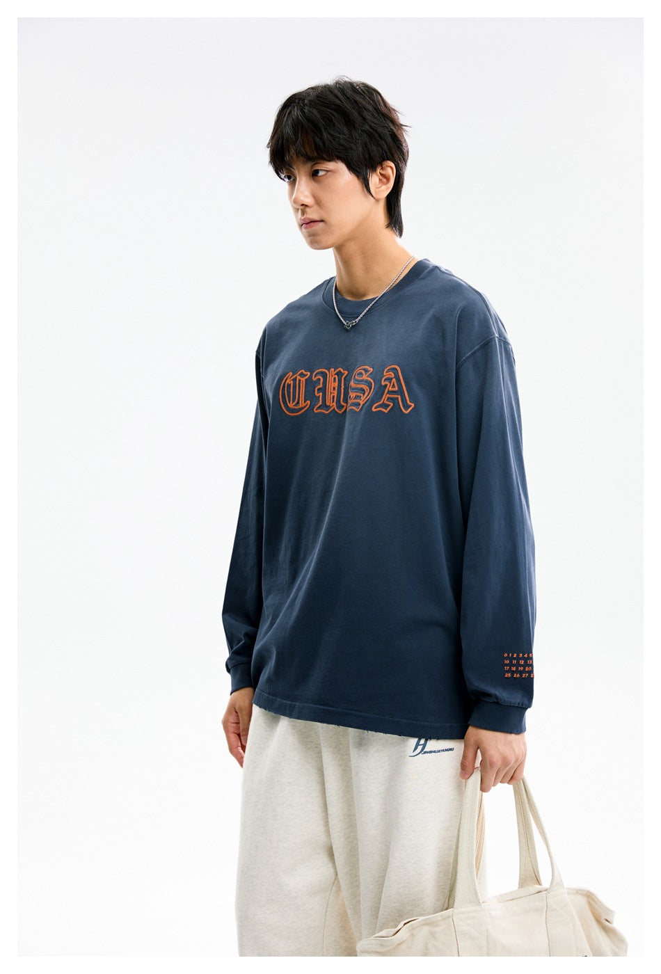 Model in a navy long-sleeve USA graphic shirt and cream pants, shown from head to upper legs.