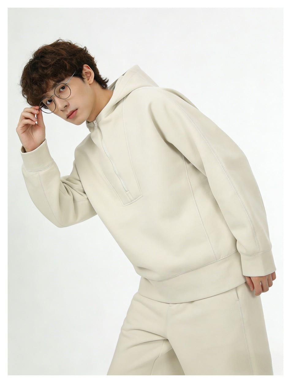 Model wearing a cream pullover hoodie with a short front zipper and matching pants.