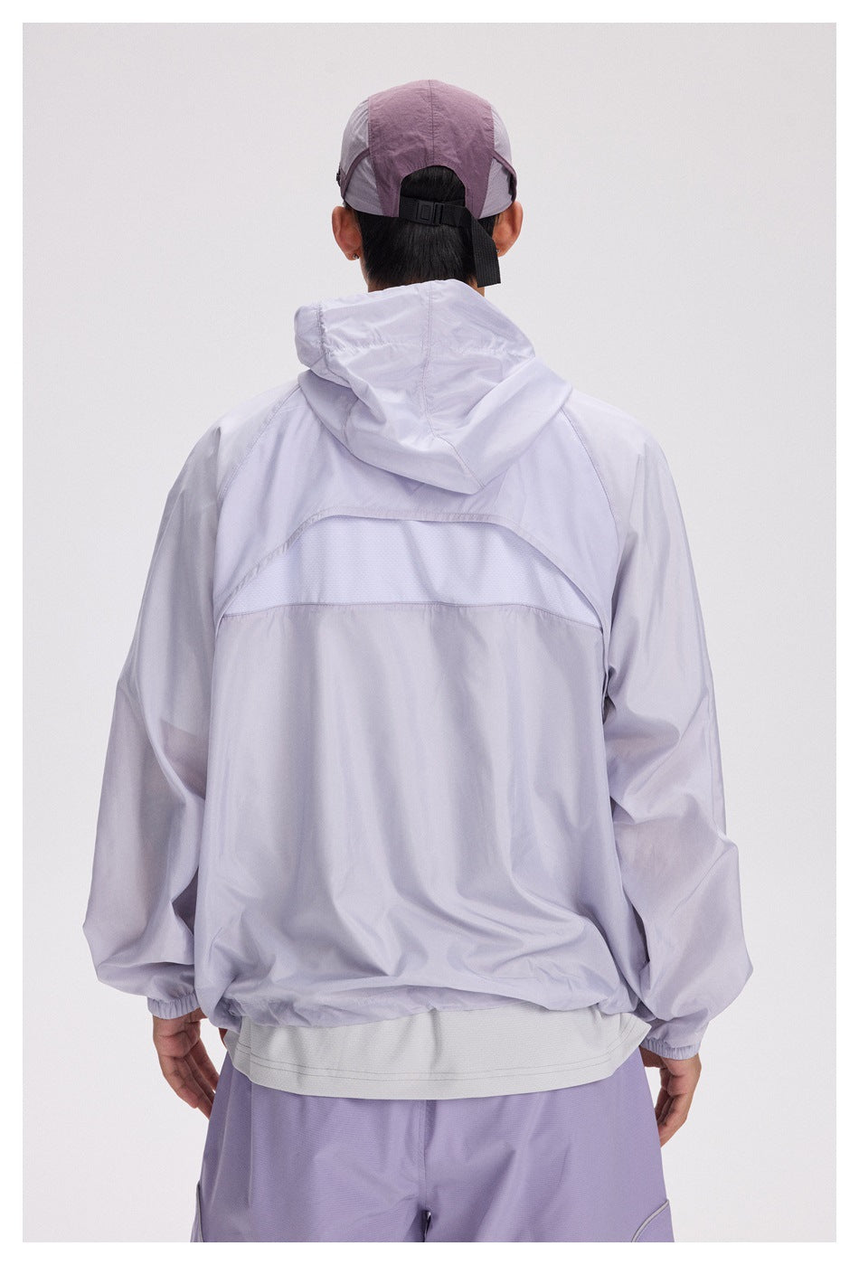 Rear view of a pale lavender hooded jacket, showing its curved mesh back panel and elastic cuffs.