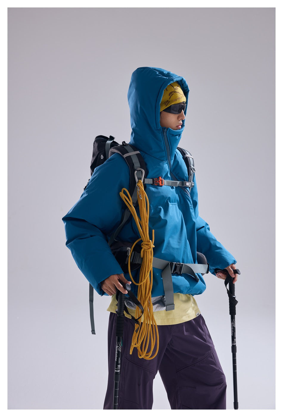 Side view of a model in a bright blue hooded pullover with hiking gear and a yellow rope.