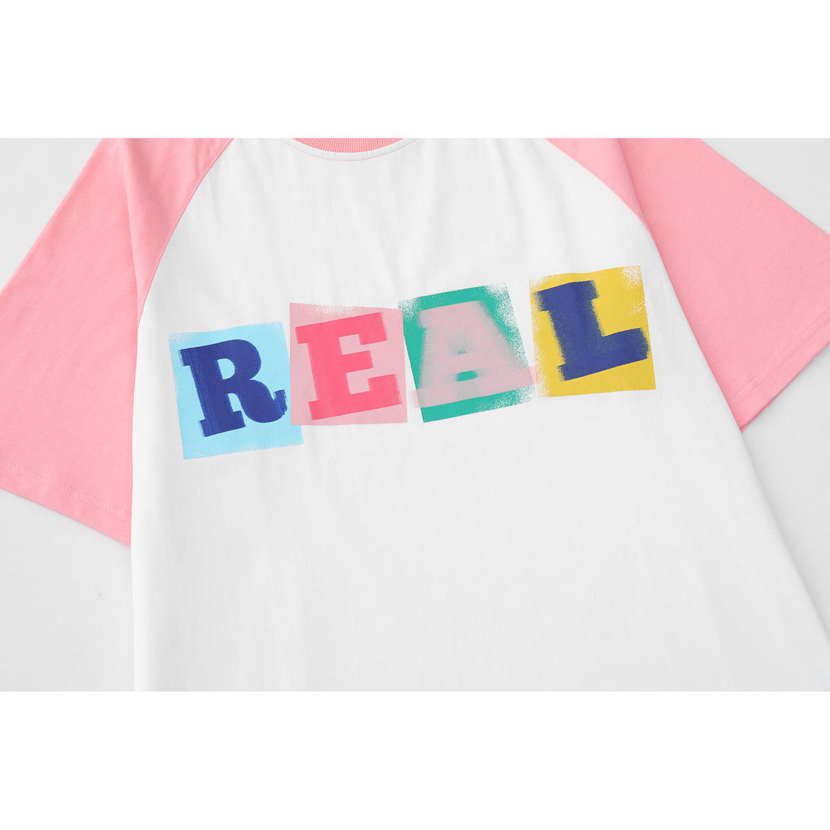 Close-up of the white T-shirt's pink raglan sleeves and colorful REAL chest print.