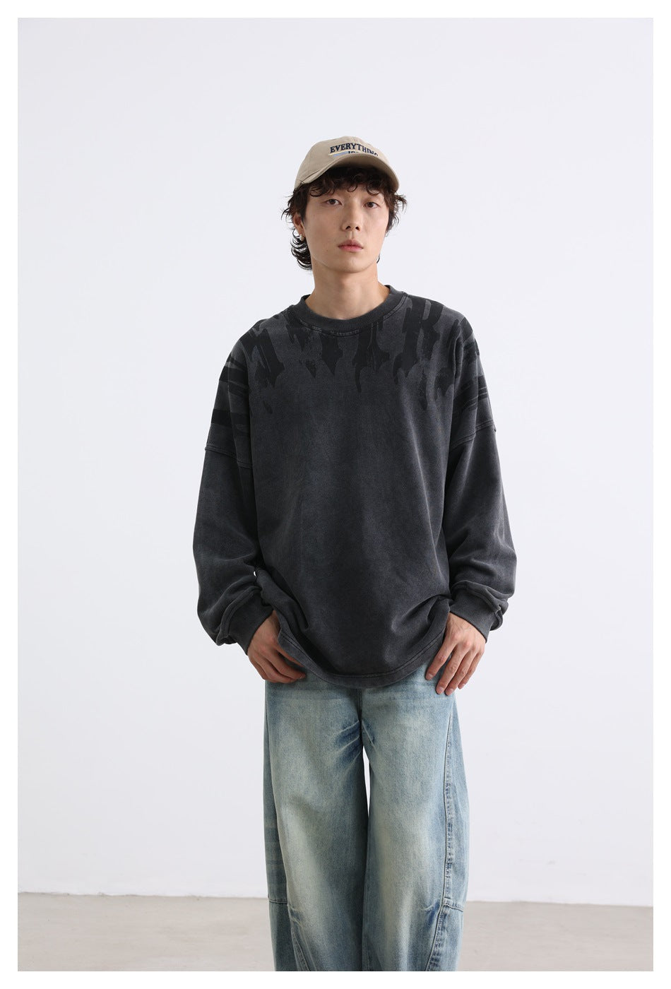 Model wearing an oversized charcoal sweatshirt with dark abstract shoulder graphics and light-wash jeans, front view.