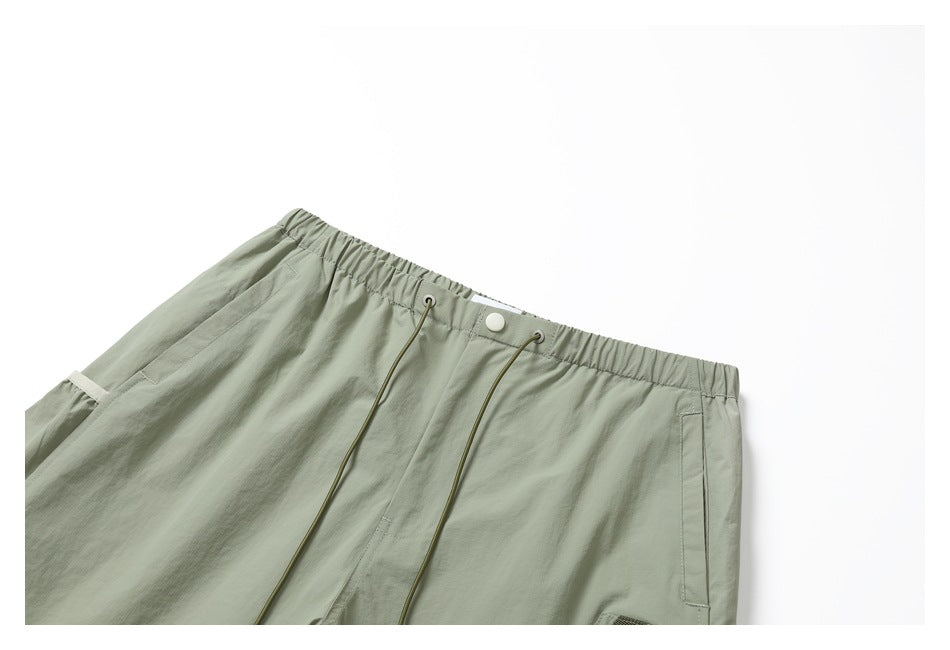 Front view of light sage utility pants with an elastic drawcord waist, snap closure, and side pockets.