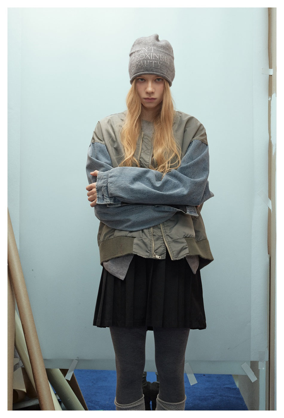 Model wearing an oversized olive-gray jacket with blue denim sleeves, shown from the front with arms crossed.
