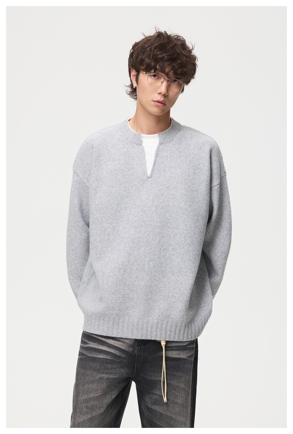 Front view of a model wearing a light gray split-neck sweater with ribbed trim and dark jeans.