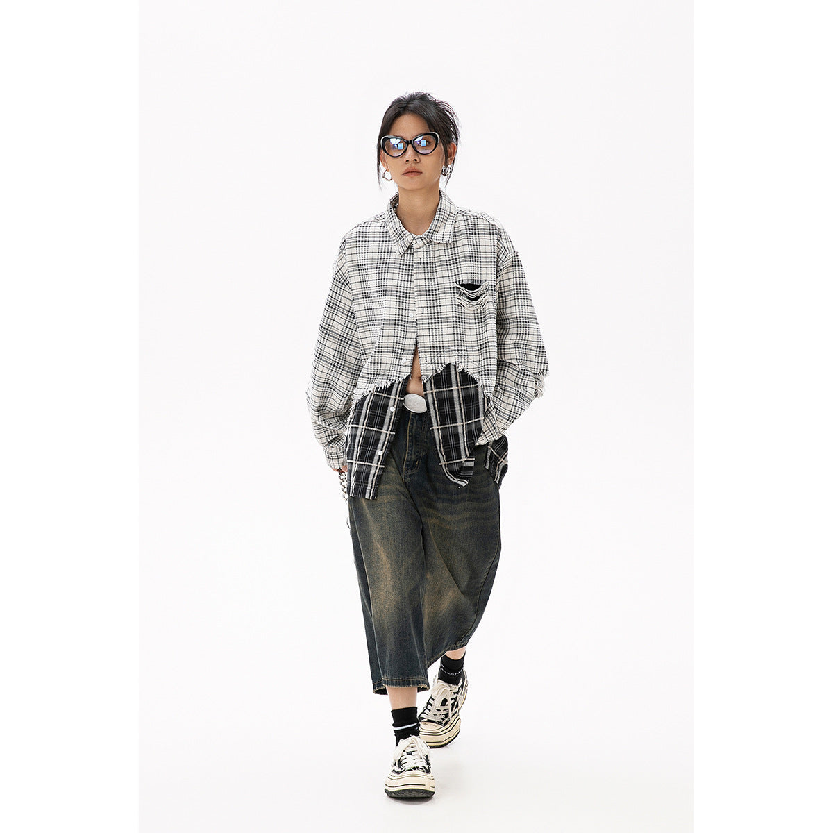 Model walking in an oversized layered black-and-white plaid shirt and dark wide-leg cropped jeans, front view.