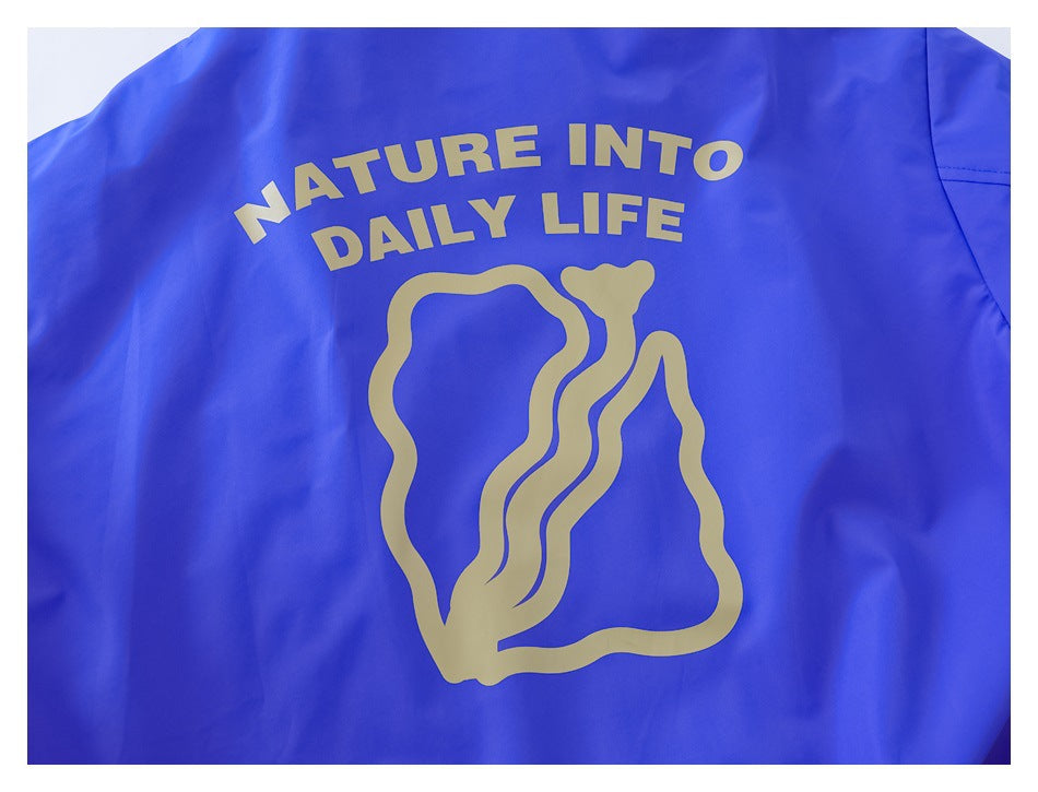 Close-up of a vivid blue garment printed with a gold abstract figure and “NATURE INTO DAILY LIFE” text.