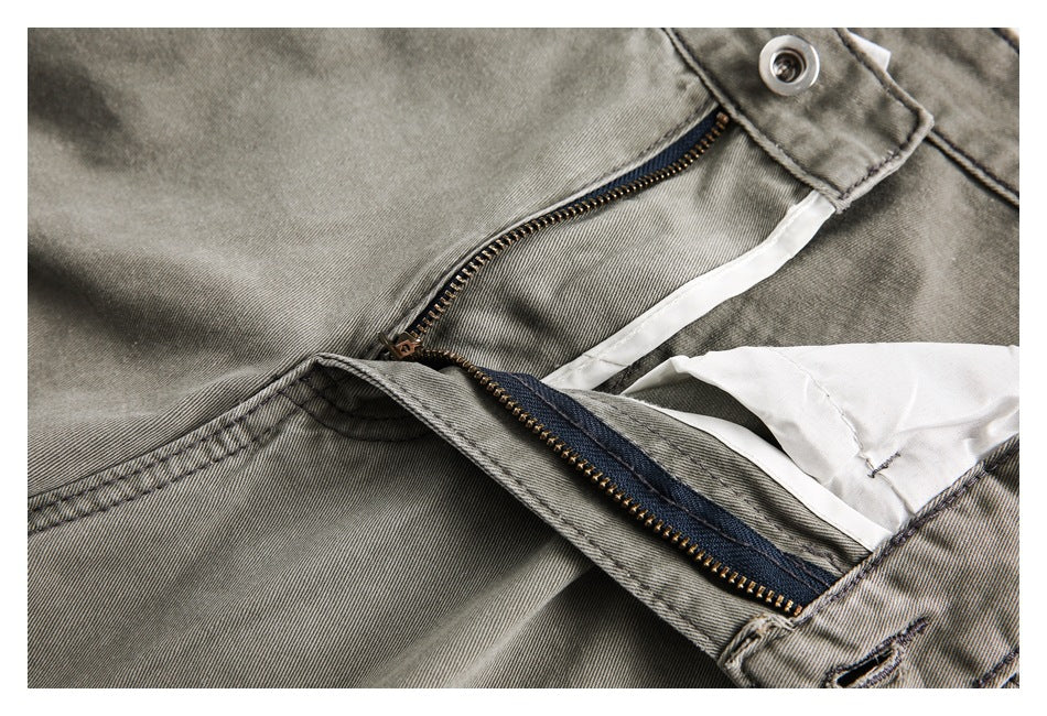Close-up of gray-olive trousers with the fly unfastened, showing the metal zipper and inner waistband.