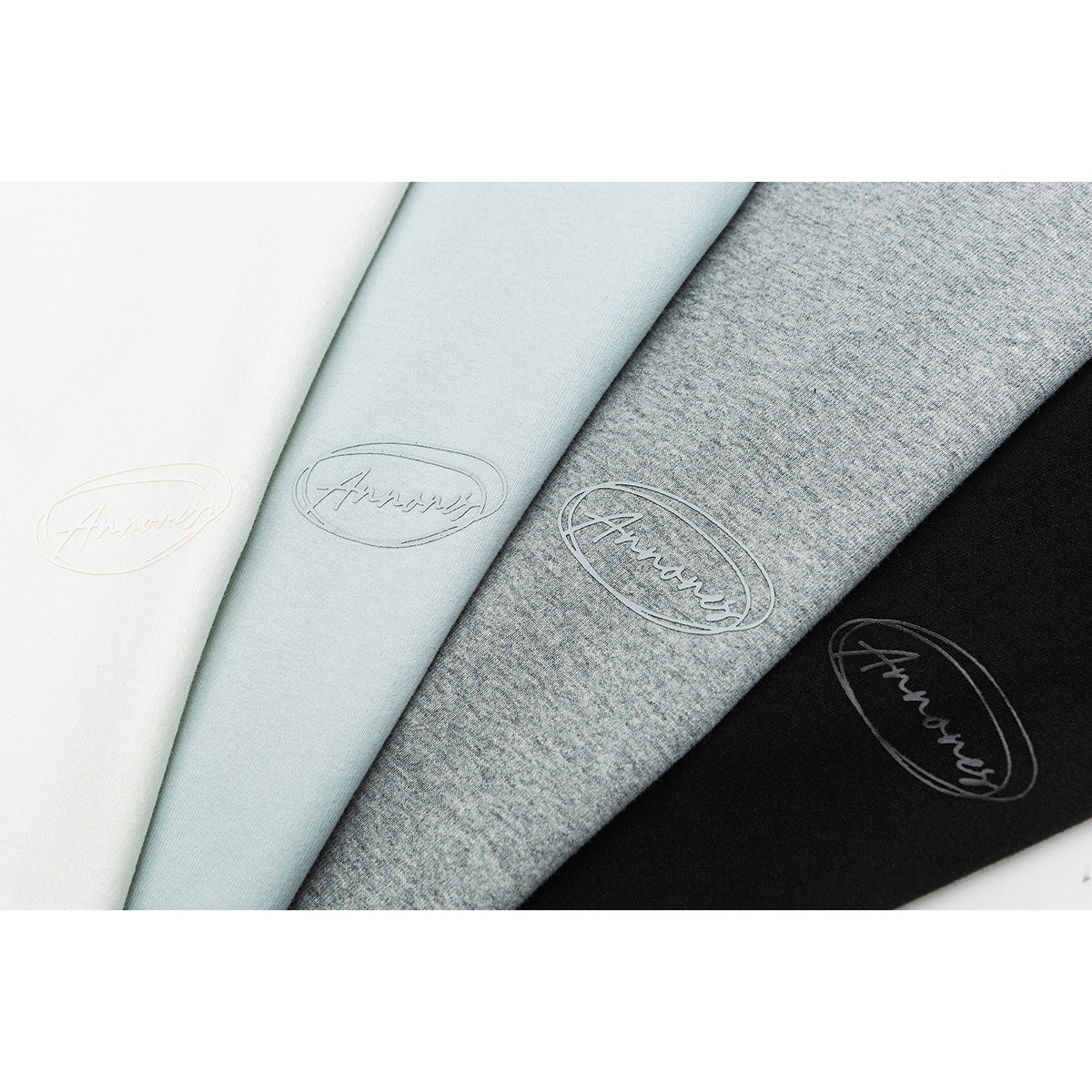 Close-up of white, pale blue, heather gray, and black T-shirt fabric with small oval script logos.