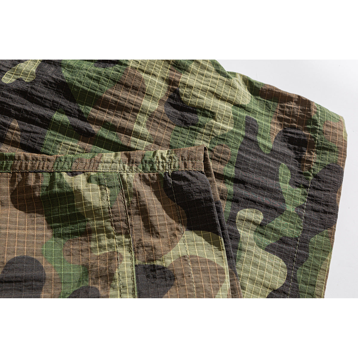 Close-up of camouflage shorts showing a large stitched cargo pocket and grid-like fabric pattern.