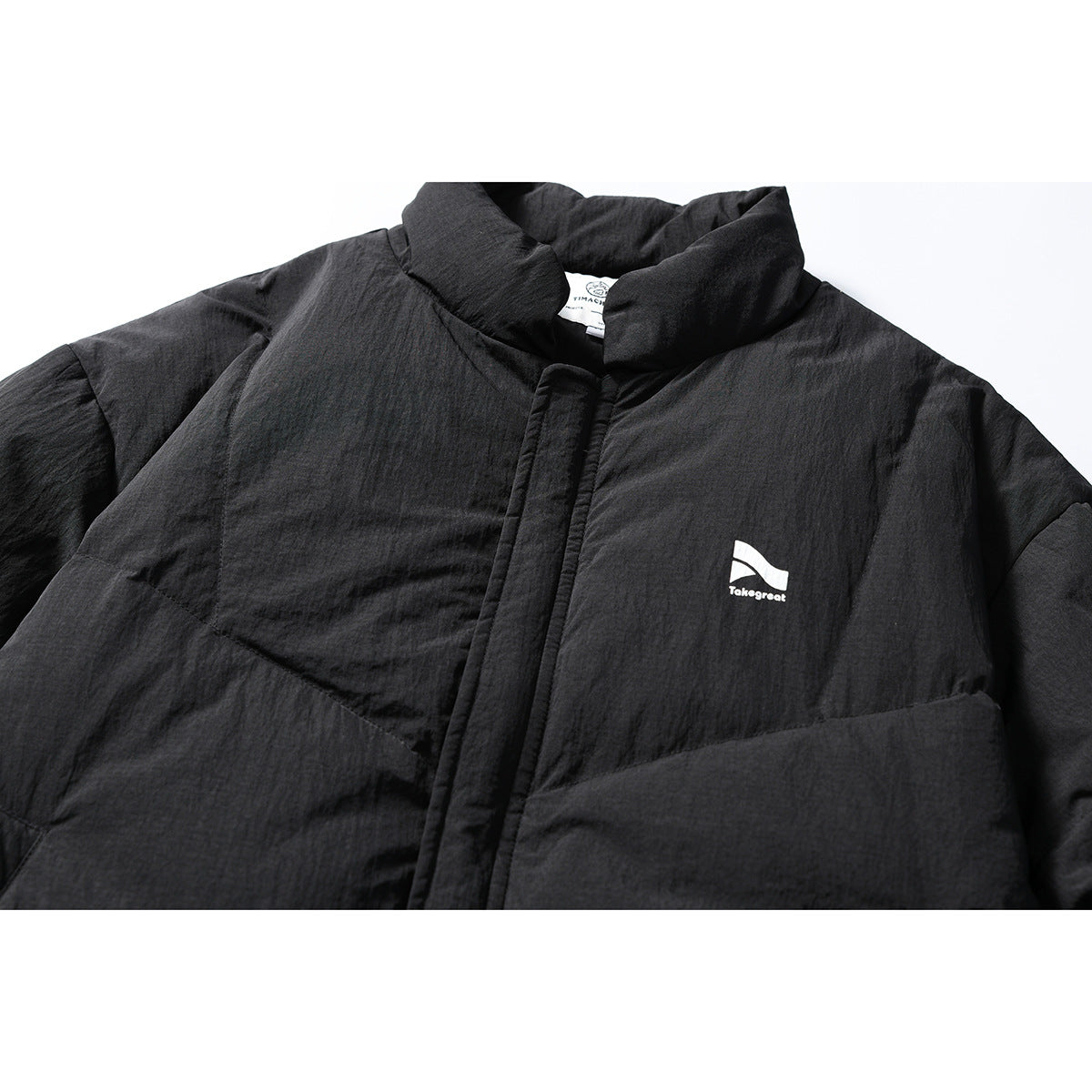 Close-up of a black quilted jacket front with a high collar, covered placket, and small white chest logo.