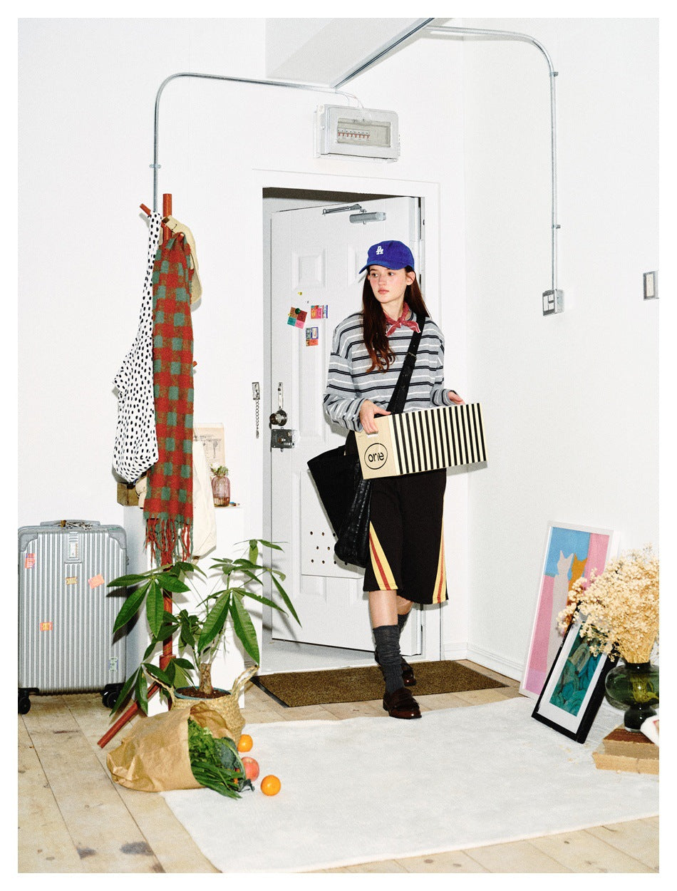 Full-length model wearing a gray striped long-sleeve shirt and black shorts with red and yellow side stripes, holding a box.