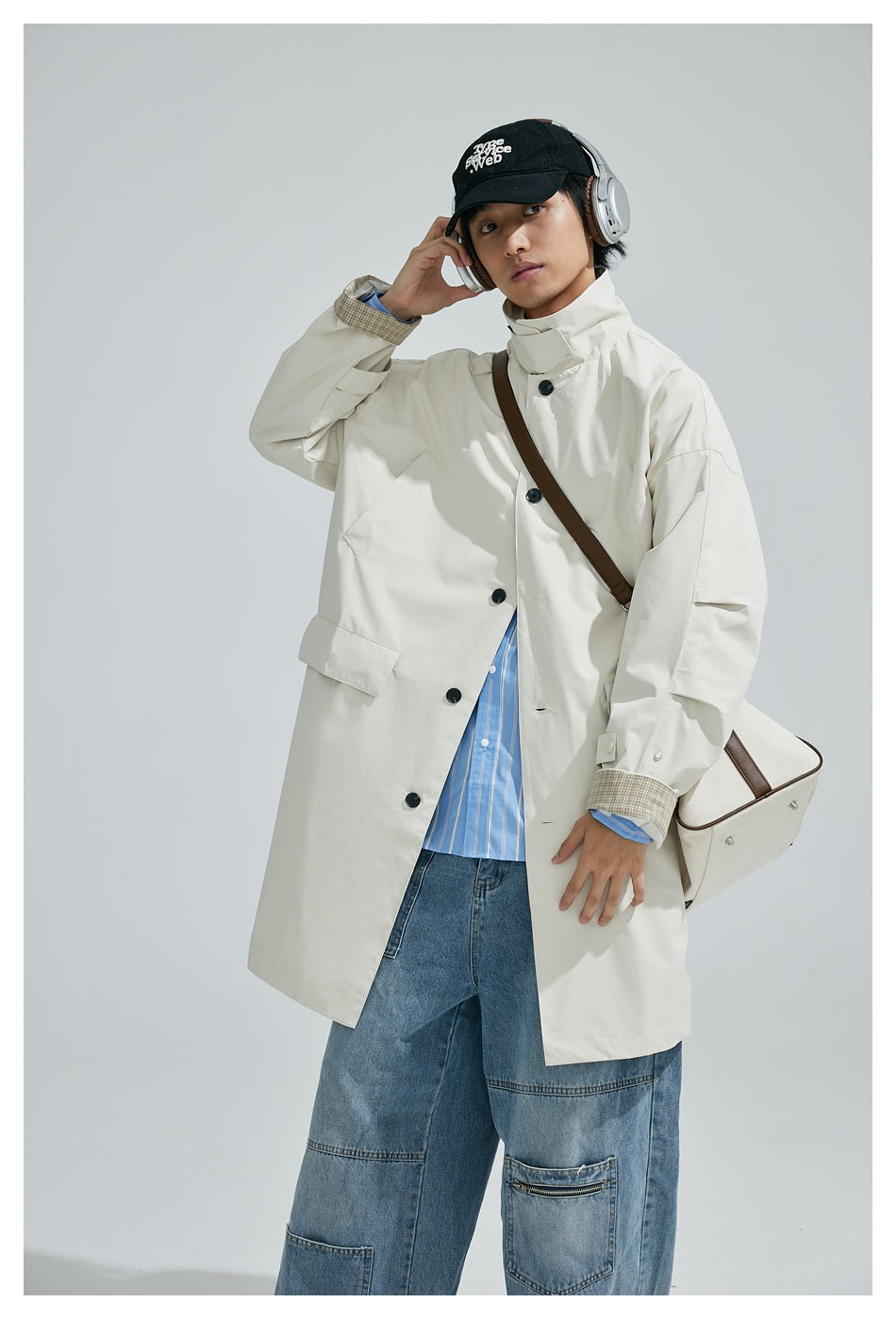 Person wearing an ivory long coat with checked cuffs over a blue striped shirt and loose jeans.