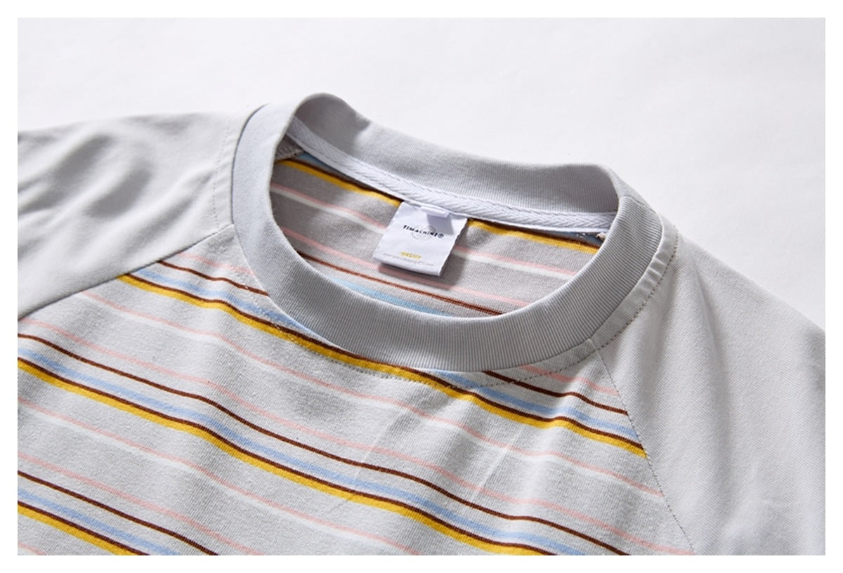 Close-up of a light gray raglan T-shirt collar and striped chest with thin yellow, blue, brown, and pink lines.