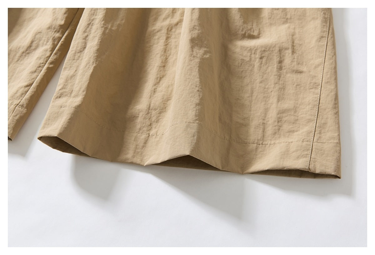 Close-up of the wide stitched hem on beige trousers laid against a white background.
