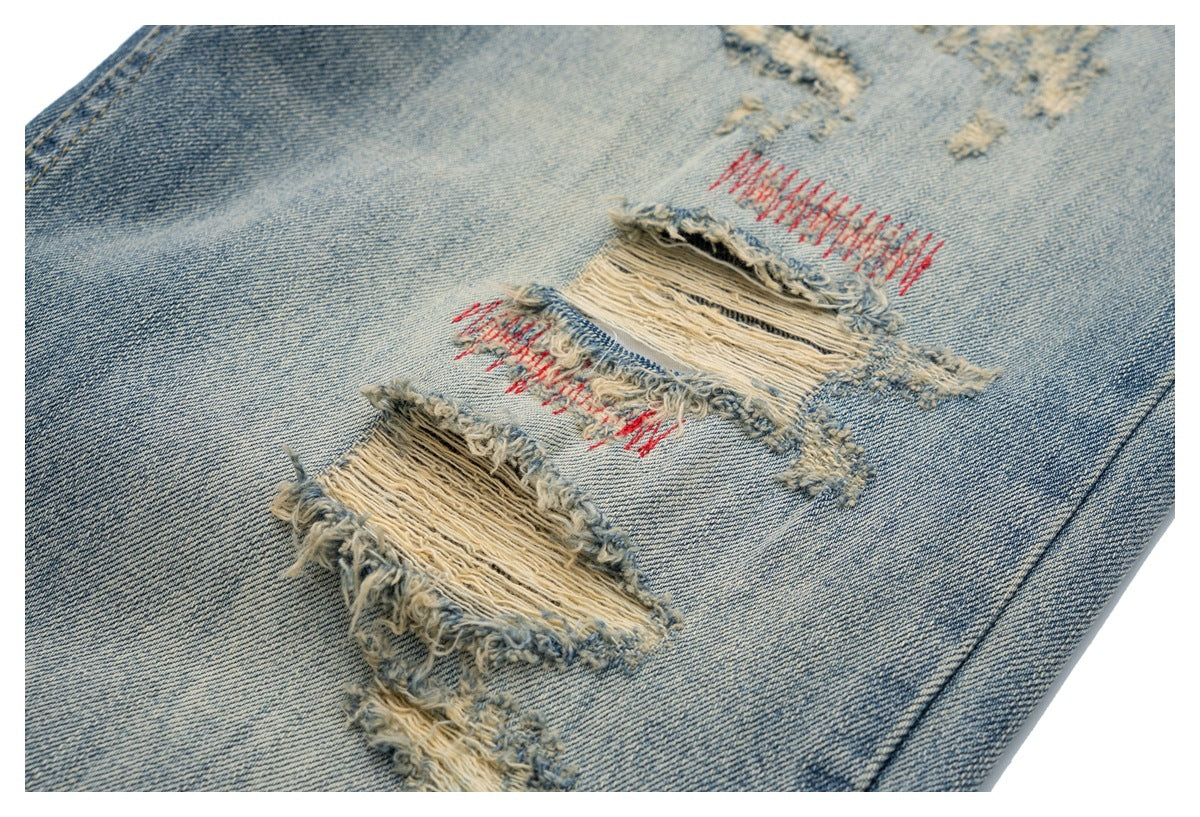 Close-up of distressed light blue jeans showing multiple frayed patches with red stitching.