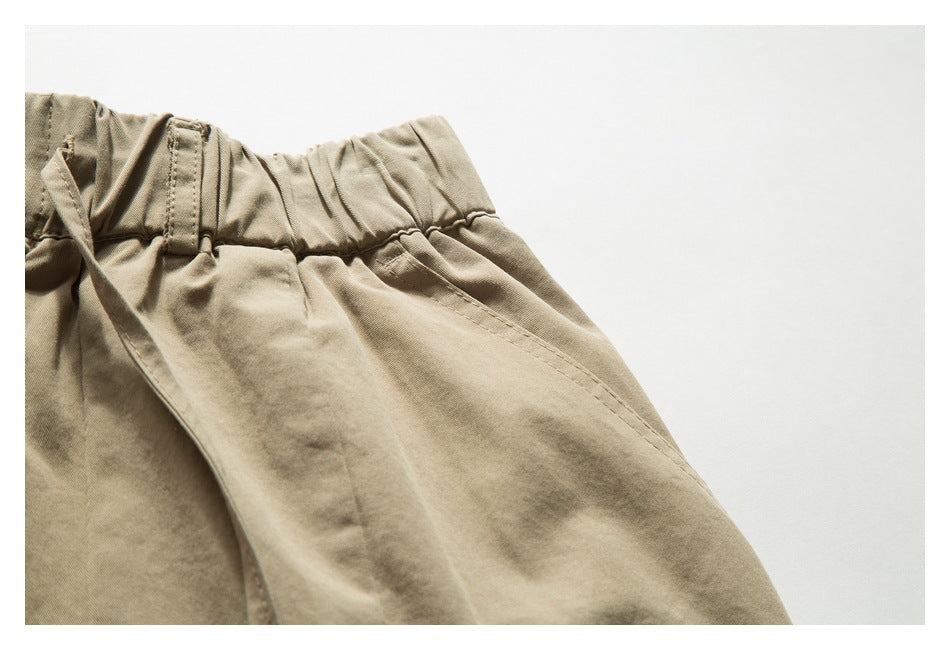 Close-up of tan trousers showing an elastic waistband, belt loop, and slanted pocket.