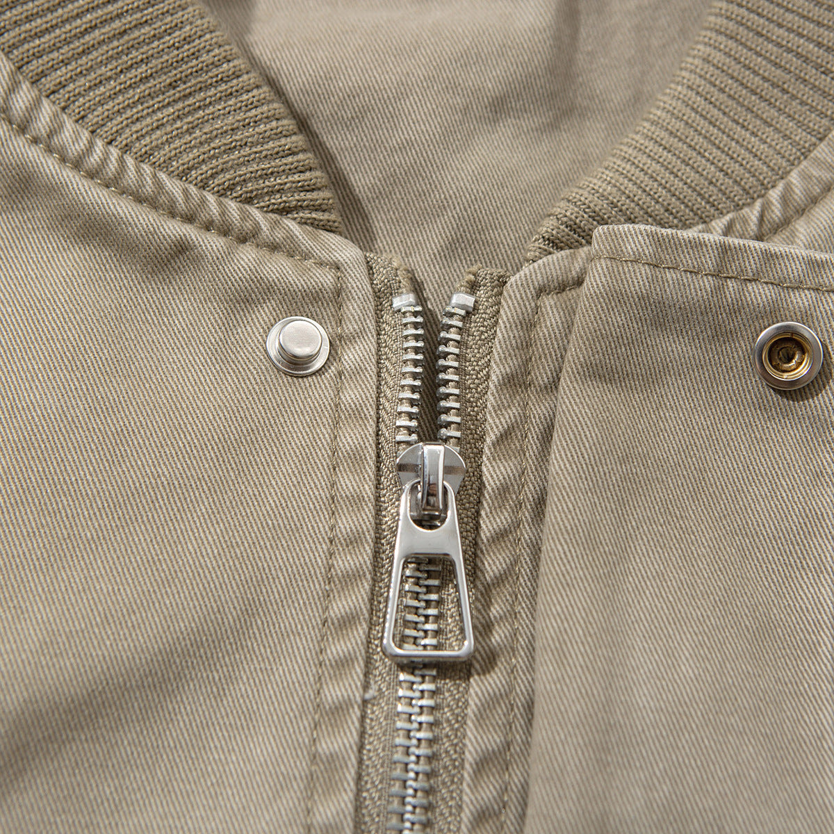 Close-up of a taupe jacket's metal front zipper, snap fasteners, and ribbed collar.